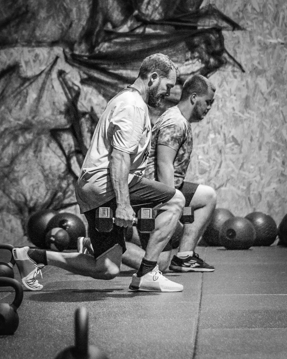 Deux hommes faisant des Lunges côte à côte en portant des haltères dans la salle de CrossFit Mazamet.