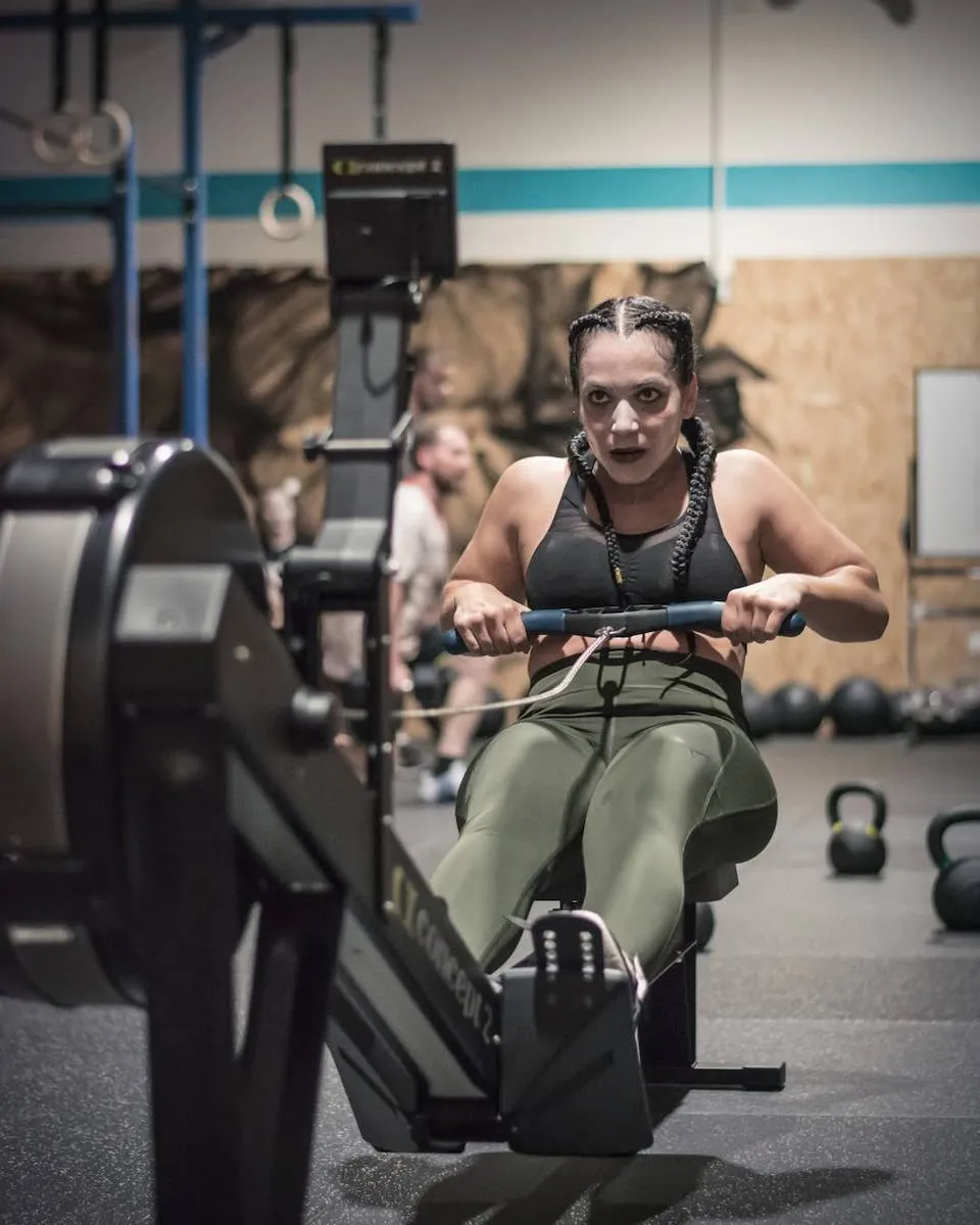 Une femme effectue un exercice de rameur lors d'une séance de préparation Hyrox.