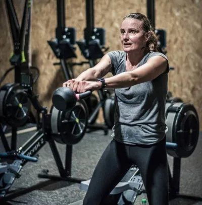 Une femme faisant un Kettle Bell Swing, devant une rangée d'ergonomes.