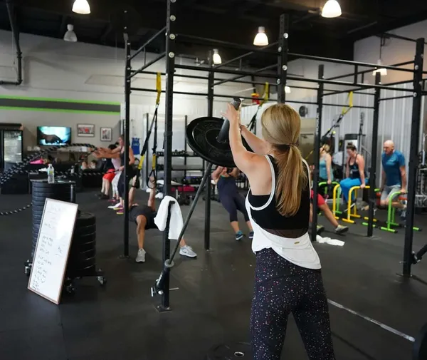 Une femme ajoutant un poids à une barre olympique dans une salle de crossfit